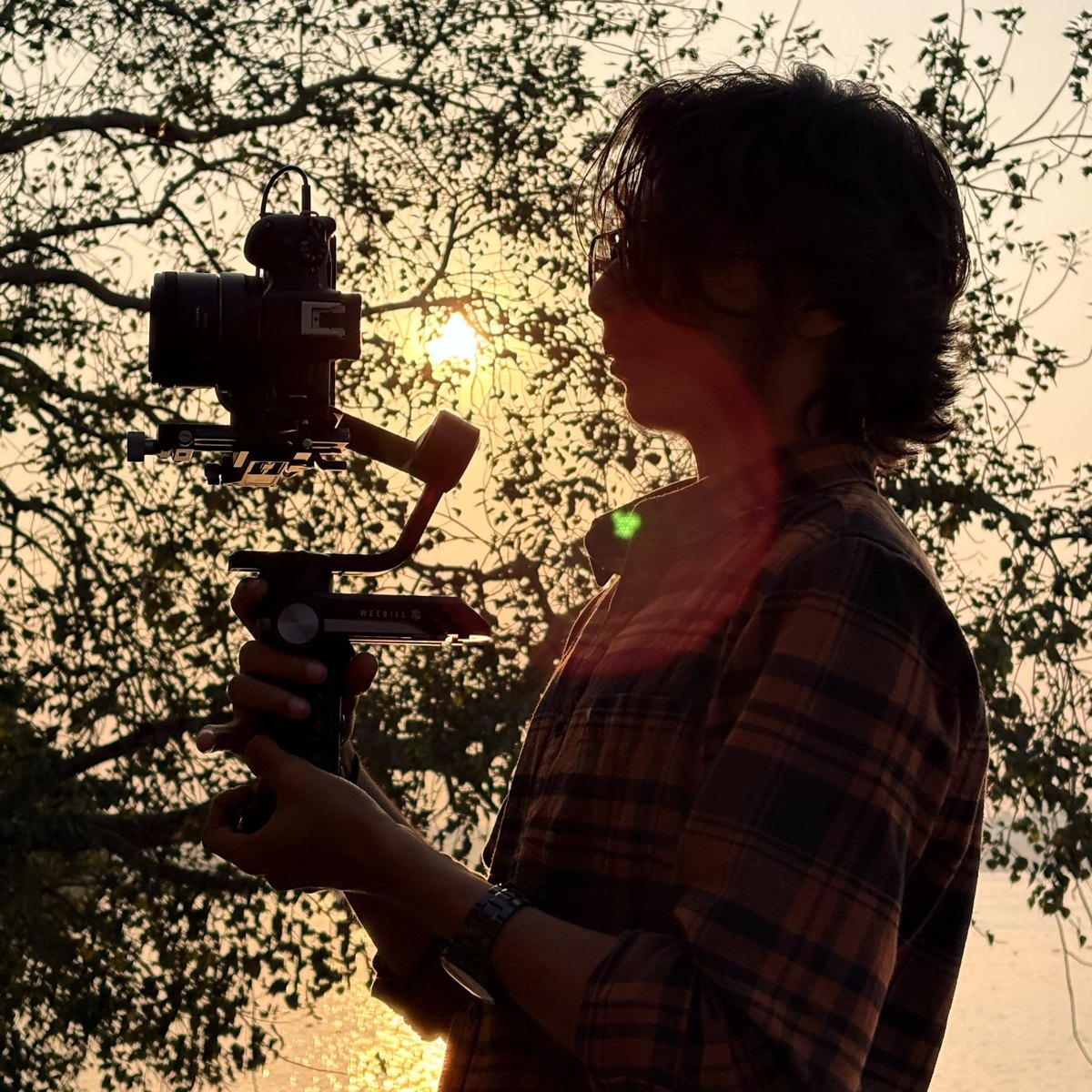 Arkadeep at the riverside at sunset, framing a shot on a gimbal-mounted camera