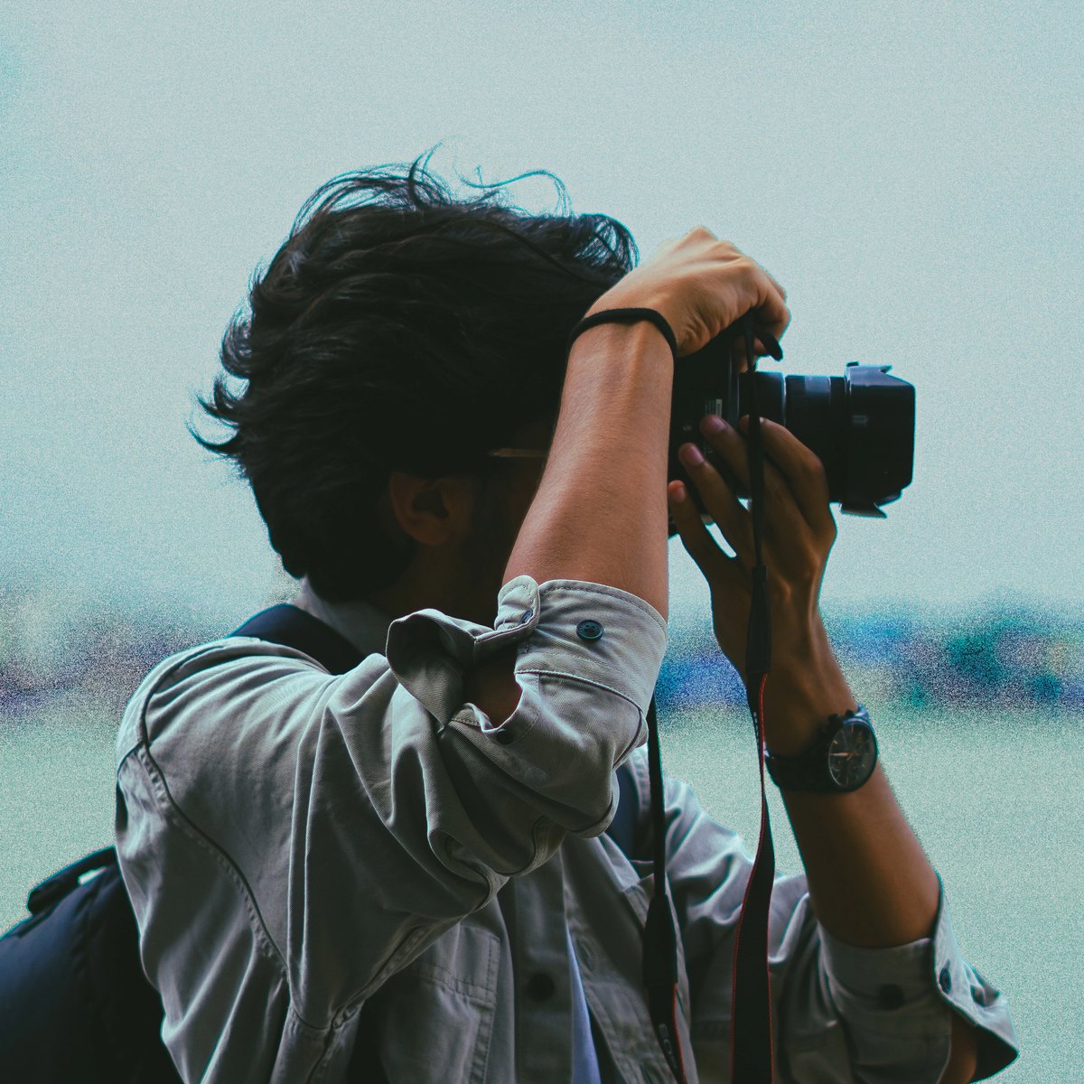 Arkadeep raising a camera to his eye against a pale sky
