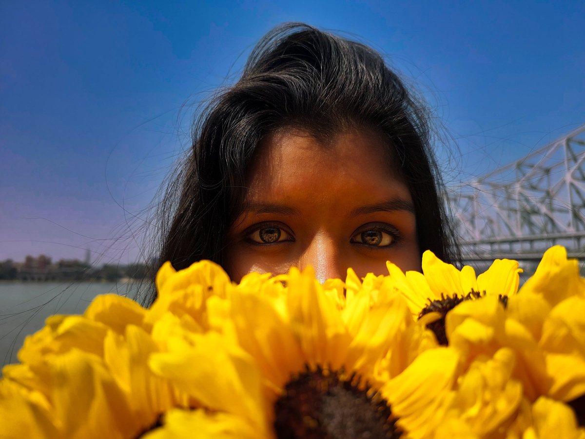 A portrait framed behind sunflowers, the Howrah Bridge behind, in black and white