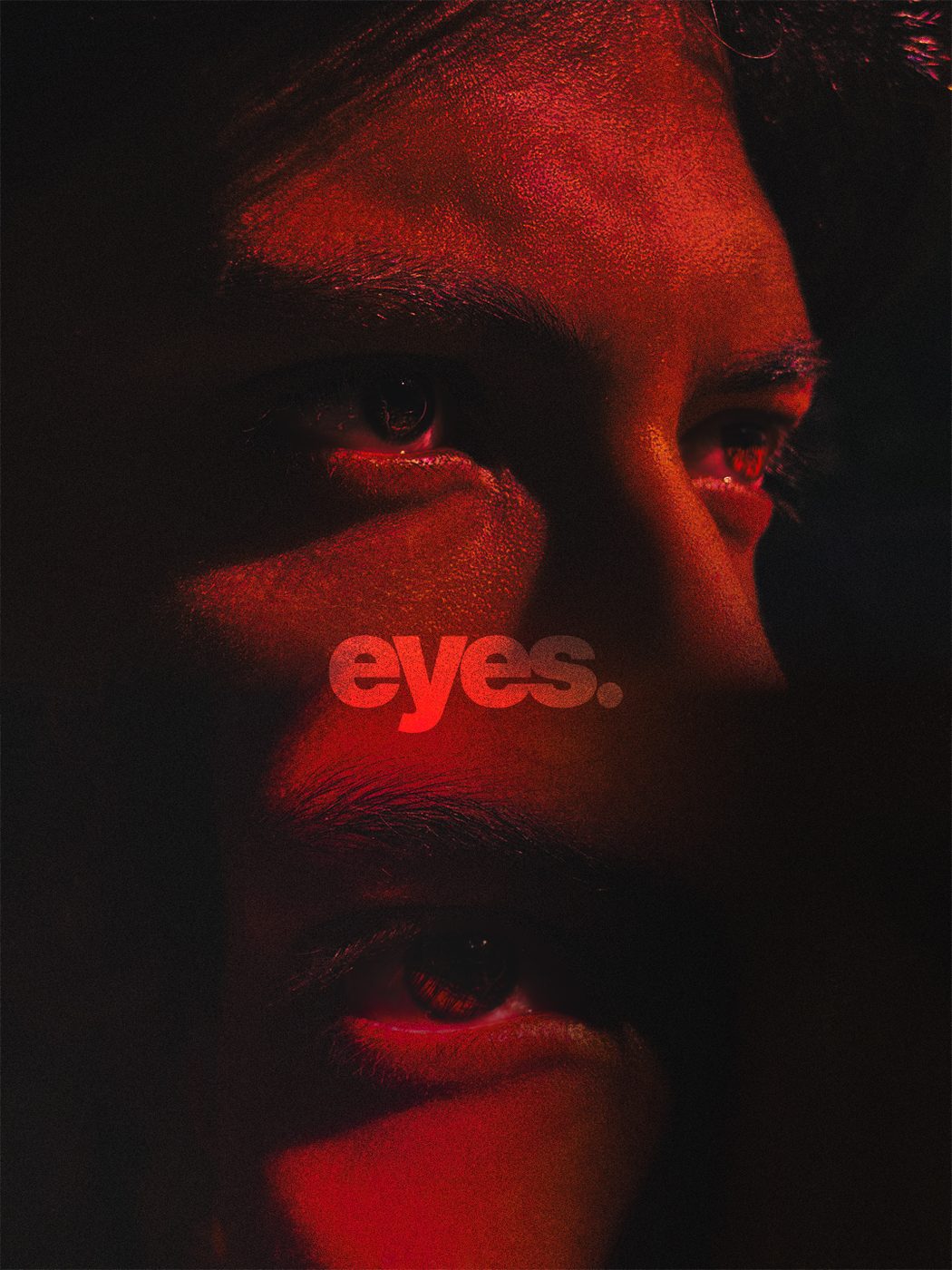 A face in deep red light, close and half in shadow, with the word eyes set across it