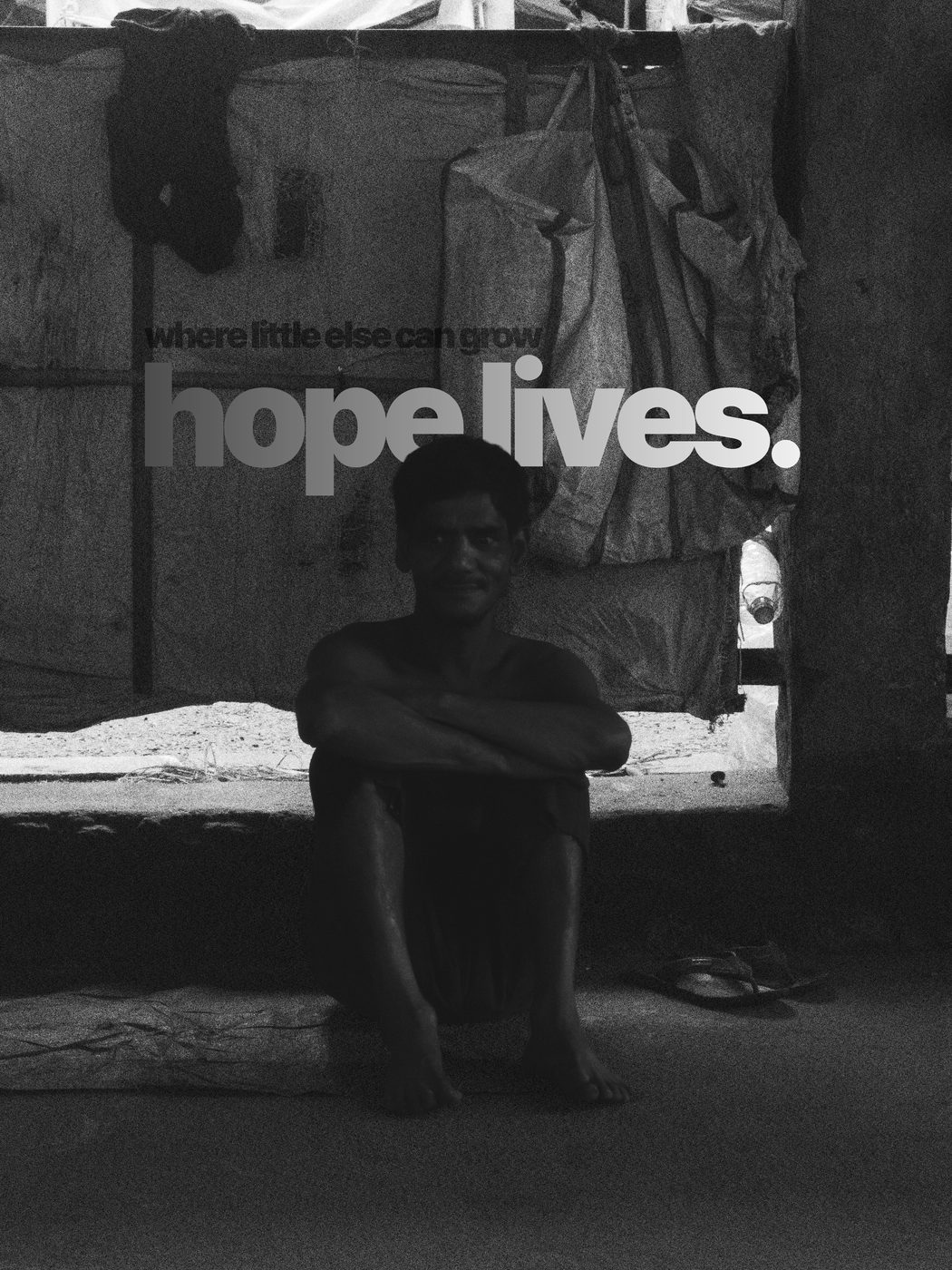 A man sitting in the doorway of a tarpaulin shack, in black and white, captioned where little else can grow, hope lives
