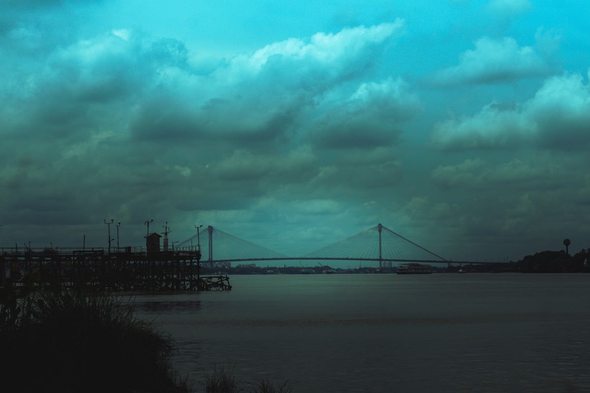The riverbank at dawn, a bridge faint in the distance
