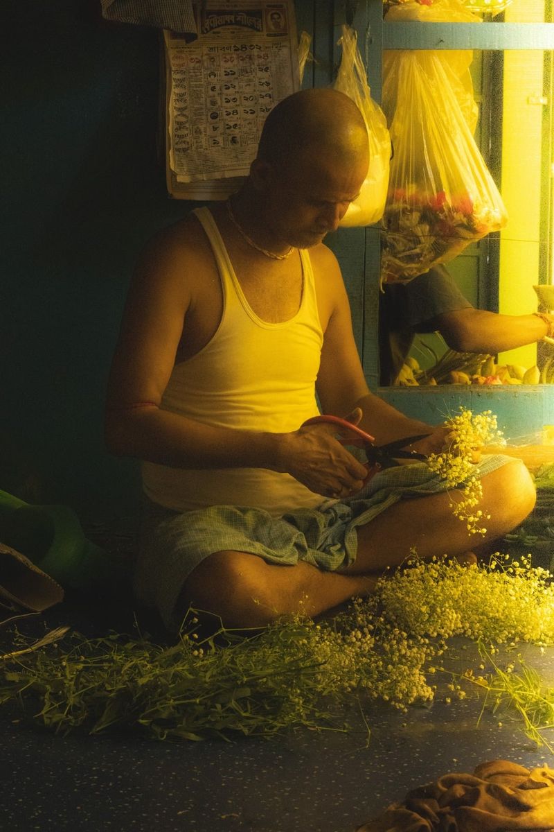 A vendor threading marigold garlands under a hanging bulb