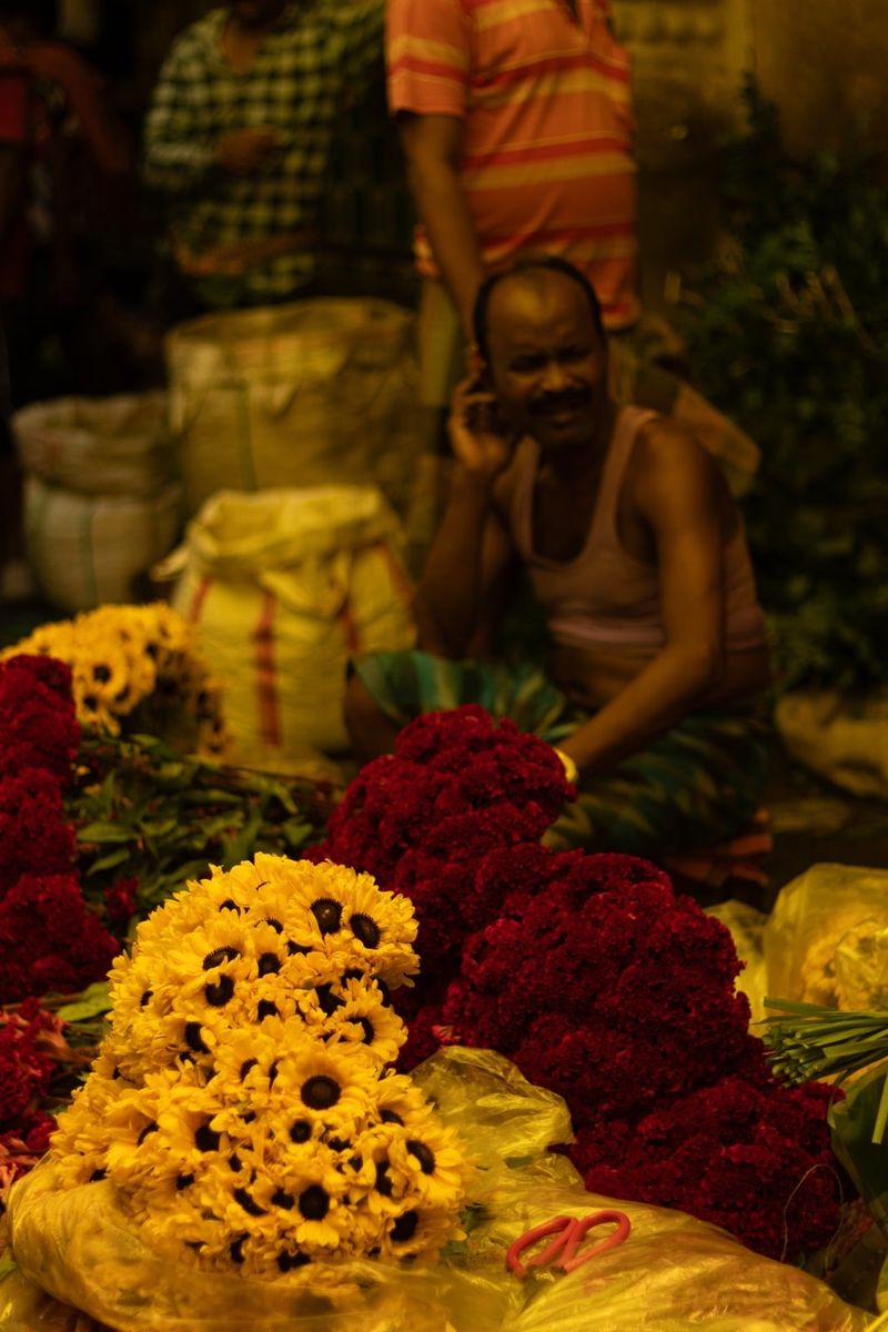 A seller behind banked marigolds and red blooms at the market